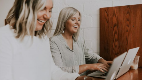 Two smiling women using laptops as an example of employee satisfaction