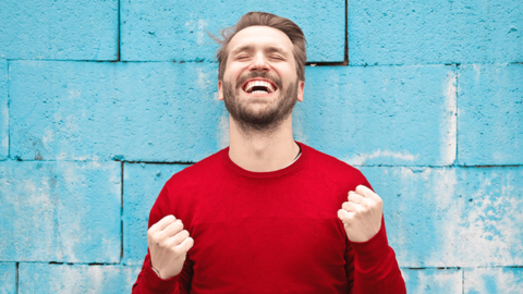 The young man wearing a red sweater is smiling with clenched fists, expressing happiness at workplace.