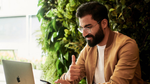 Photo of a man on an online meeting looking at his laptop and showing a thumbs up symbolizing that he agrees to something that was said in the meeting