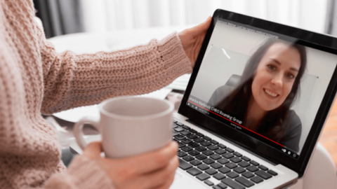 The woman is watching the webinar 'People as the Company's Greatest Asset 'on her laptop while holding a cup of coffee