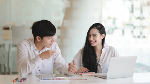 The smiling woman and man sitting together in front of laptop, collaborating to present a positive company culture