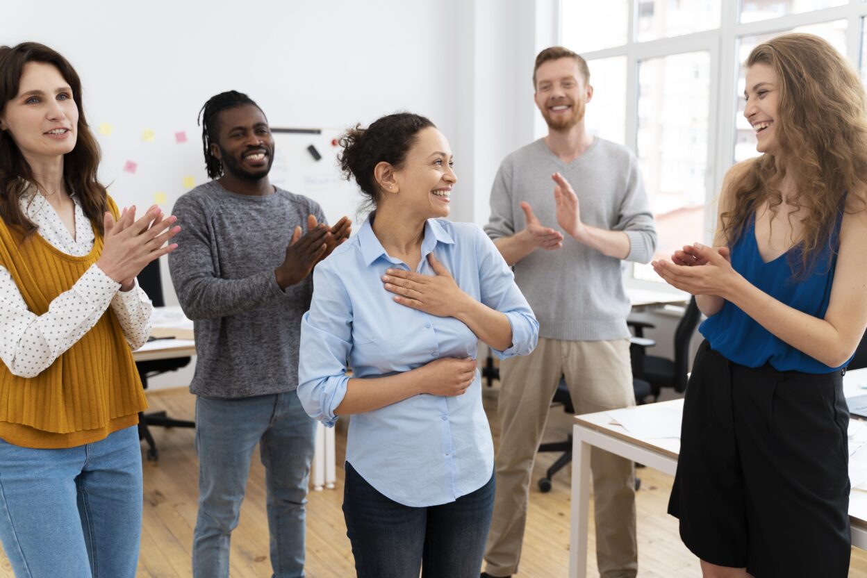 Team members giving peer recognition by applauding a colleague during a team meeting in the office