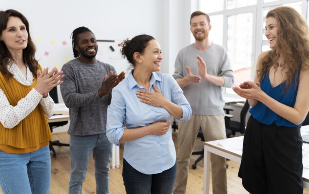 Team members giving peer recognition by applauding a colleague during a team meeting in the office