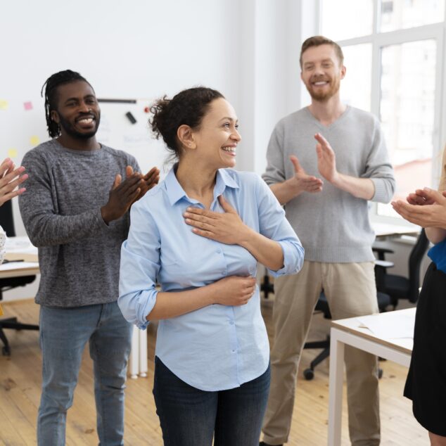 Team members giving peer recognition by applauding a colleague during a team meeting in the office